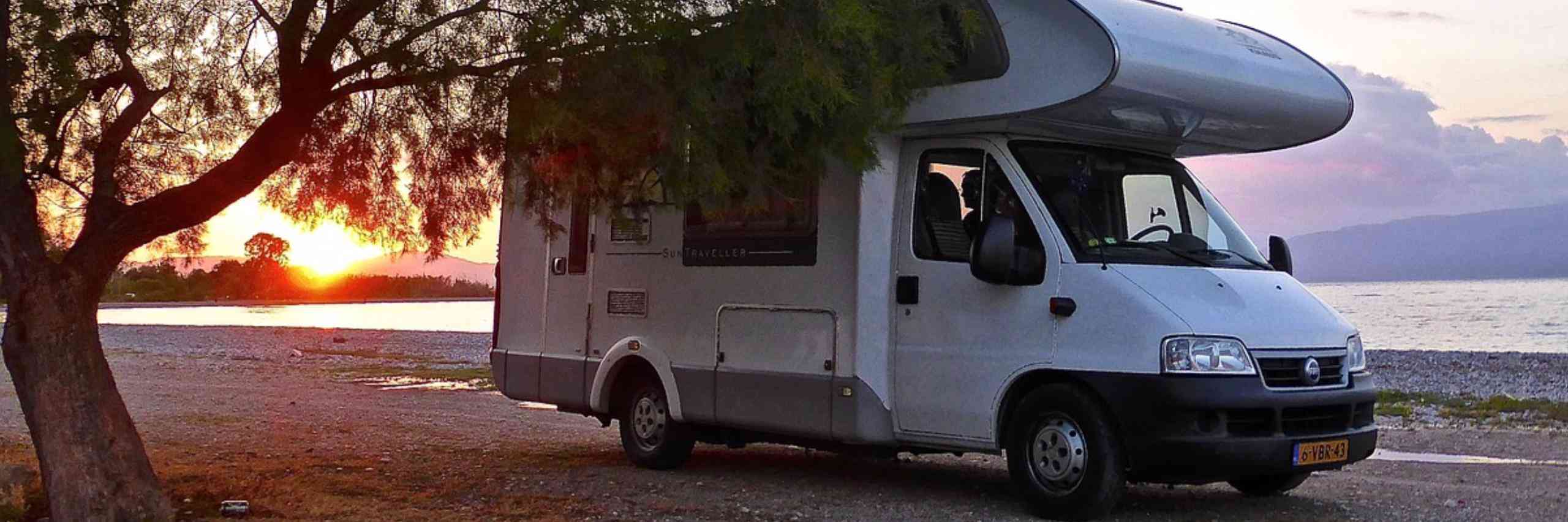 RV camper parked beside tree and lake